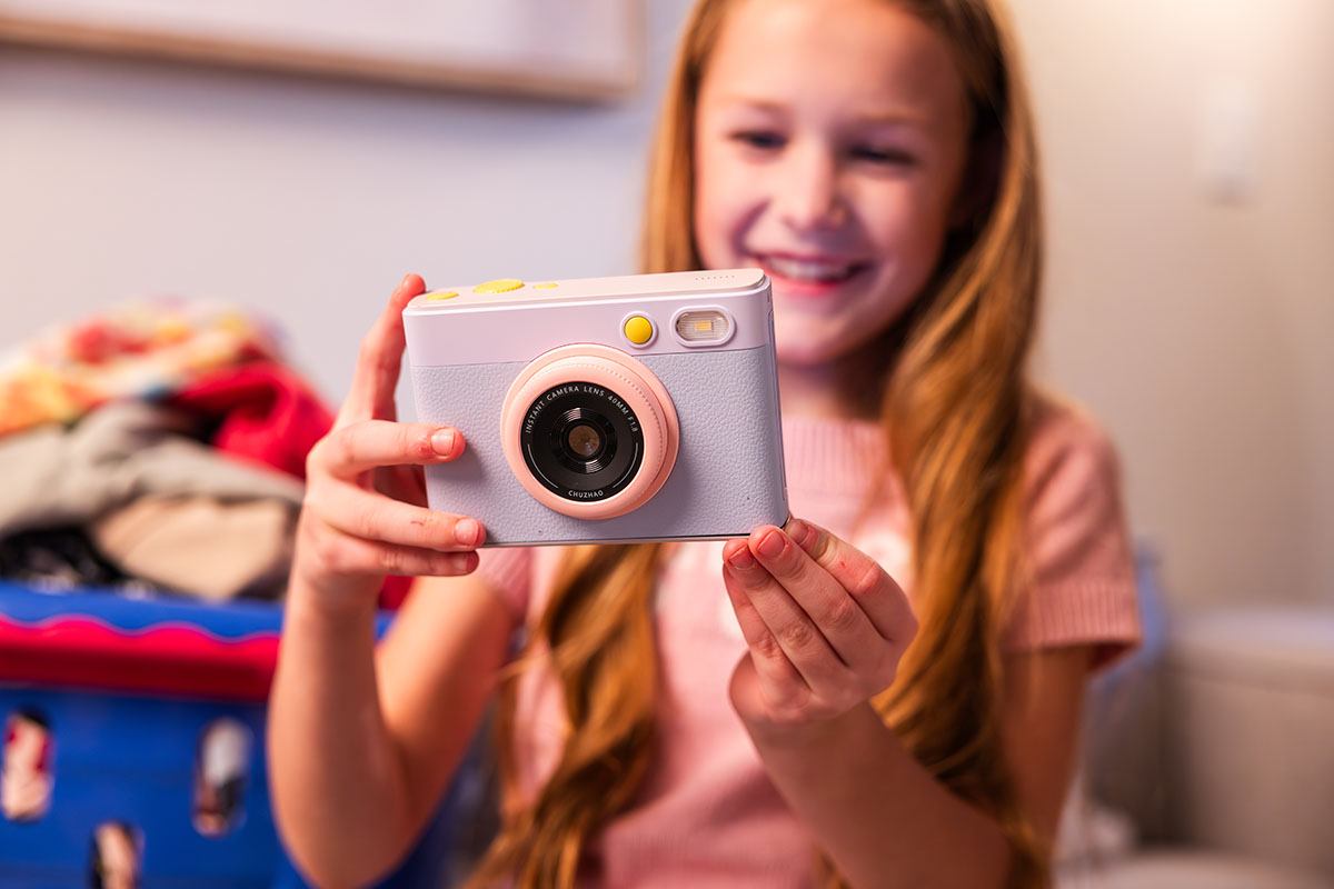 A little blonde girl holding a pink and purple instant print camera