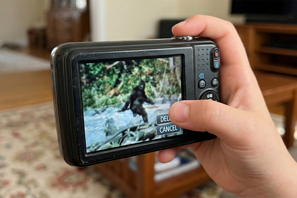A child holding a camera displaying a blurry picture of Bigfoot